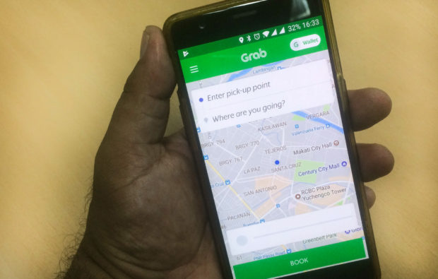 Closeup of smartphone that shows Grab app. STORY: For TNVS drivers, fuel price hikes mean longer hours