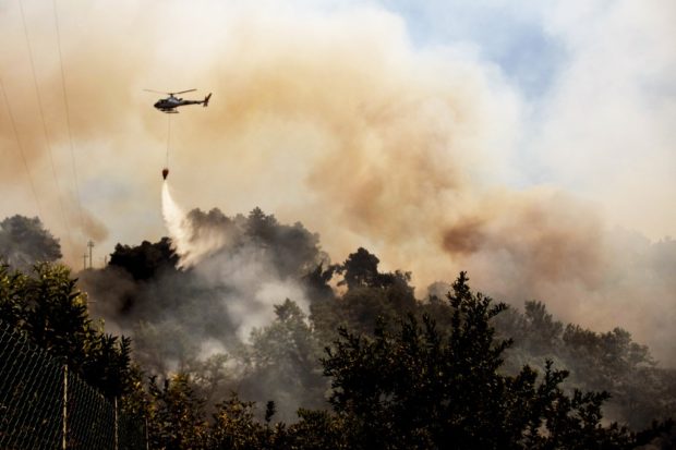 An helicopter drops water over a wildfire raging near the city of Massarosa, Tuscany region, central Italy, on July 20, 2022. 