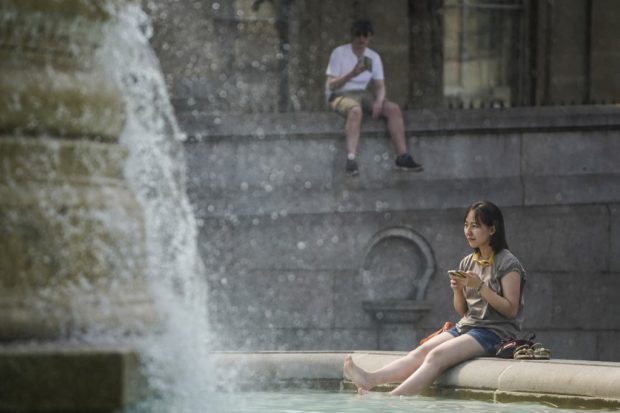 A woman cools off by dipping her feet in the fountain of Trafalgar Square, in central London, on July 18, 2022 as the country experiences an extreme heat wave.