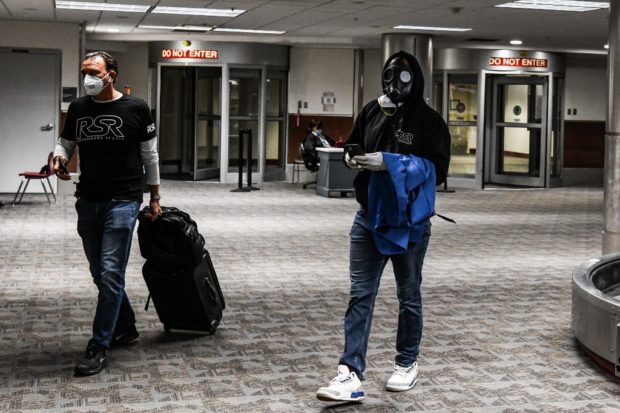 A man wear a gasmask (R) as he arrives at Hartsfield-Jackson Atlanta International Airport in Atlanta, on April 23, 2020. - The US Treasury is providing aid to the airlines as part of the $2.2 trillion stimulus legislation approved last month, as the coronavirus pandemic hits the travel industry. (Photo by CHANDAN KHANNA / AFP)