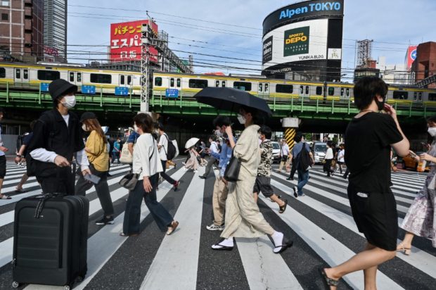 People cross the street in the Shinjuku district of Tokyo on August 16, 2022. (Photo by Richard A. Brooks / AFP)
