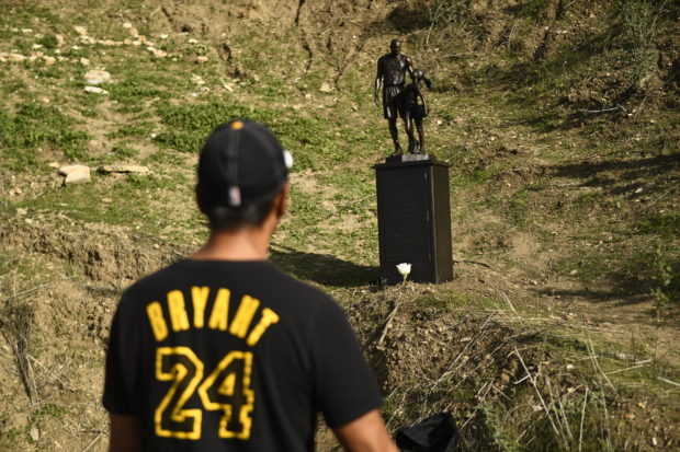 A person looks at a bronze sculpture by artist Dan Medina, depicting Kobe Bryant, daughter Gianna Bryant, and the names of those who died, during a one-day temporary memorial at the site of a 2020 helicopter crash in Calabasas, California, on January 26, 2022. - Lakers star Kobe Bryant died with his daughter Gianna in a tragic helicopter crash which killed nine people on January 27, 2020. (Photo by Patrick T. FALLON / AFP) / RESTRICTED TO EDITORIAL USE - MANDATORY MENTION OF THE ARTIST UPON PUBLICATION - TO ILLUSTRATE THE EVENT AS SPECIFIED IN THE CAPTION