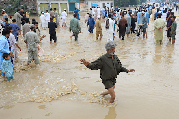 A man balances himself as he, along with others, walks on a flooded road, following rains and floods during the monsoon season in Charsadda. STORY: Pakistan floods force tens of thousands from homes overnight