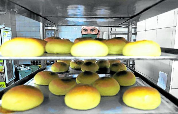 Pandesal on trays in a bakery with a baker peeking from behind. STORY: DTI: Wheat prices have been going down since May