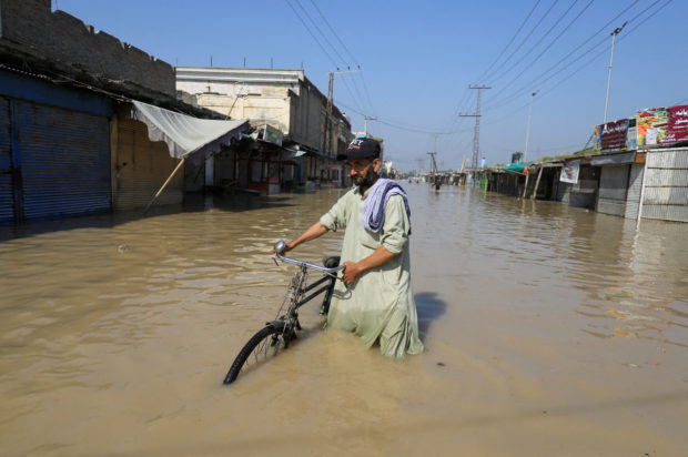 A man walks with a bicycle in flood water following rains and floods during the monsoon season in Nowshera, Pakistan August 29, 2022. REUTERS/Fayaz Aziz