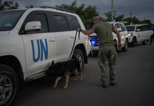 Ukrainian serviceman with a dog checks a motorcade transporting a part of the International Atomic Energy Agency (IAEA) mission coming back from a Zaporizhzhia nuclear power plant, amid Russia's invasion of Ukraine, at a Ukrainian checkpoint in Zaporizhzhia region, Ukraine September 1, 2022. REUTERS/Anna Voitenko