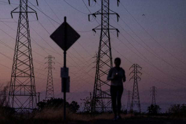 FILE PHOTO: A woman jogs by power lines, as California's grid operator urged the state's 40 million people to ratchet down the use of electricity in homes and businesses as a wave of extreme heat settled over much of the state, in Mountain View, California, U.S., August 17, 2022. REUTERS/Carlos Barria