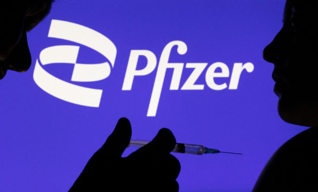 FILE PHOTO: People pose with syringe with needle in front of displayed Pfizer logo in this illustration taken, December 11, 2021. REUTERS/Dado Ruvic/Illustration