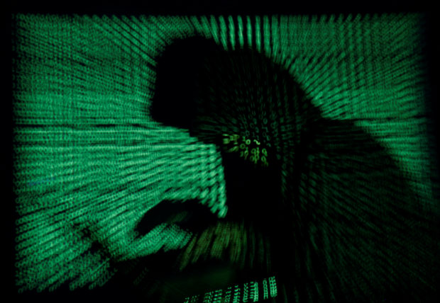 FILE PHOTO: A hooded man holds a laptop computer as cyber code is projected on him in this illustration picture taken on May 13, 2017. Top U.S. fuel pipeline operator Colonial Pipeline has shut its entire network after a cyber attack, the company said on Friday. REUTERS/Kacper Pempel/Illustration/