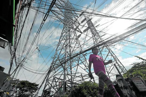 A woman walks past a transmission tower in Caloocan City as the alert status of the Luzon power grid is raised from yellow to red on Monday. Electricity supply in the past few days was insufficient to meet the demand, as several plants broke down. —GRIG C. MONTEGRANDE FOR STORY: Brownouts hit Luzon as 7 power plants shut down