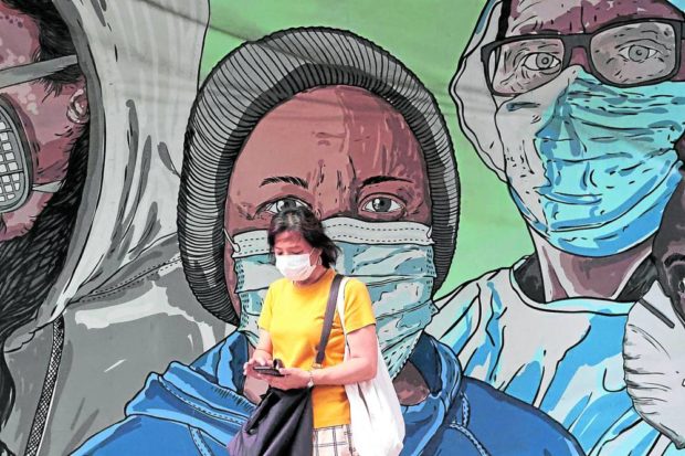 Pedestrian with a cellphone in front of a mural of people in face masks. STORY: DOH: Wearing of masks still voluntary