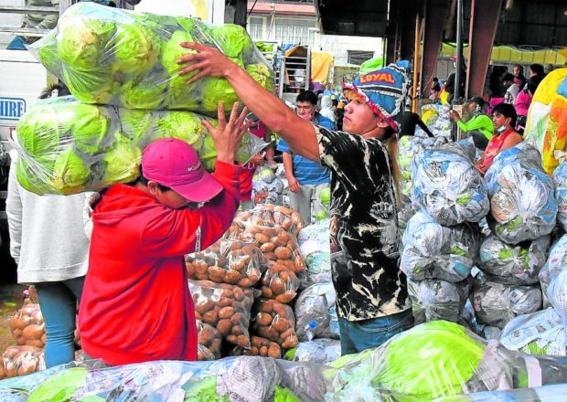 Man in market helping another man with bags of lettuce on his shoulder. STORY: Cordillera reels from rising inflation
