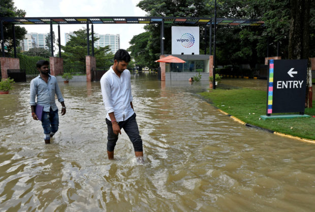 People wade through a waterlogged road in front of the entrance of IT major Wipro Ltd following torrential rains in Bengaluru, India, September 5, 2022. REUTERS/Samuel Rajkumar/File Photo