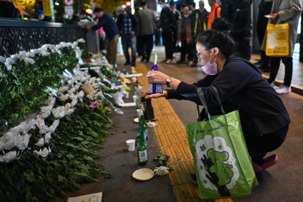 A woman makes an offering, in tribute to those killed in a Halloween stampede on October 29, at a makeshift memorial outside the Itaewon subway station in the district of Itaewon in Seoul on October 30, 2022. - More than 150 people were killed in a stampede at a Halloween event in central Seoul, officials said on October 30, with South Korea's president vowing a full investigation into one of the country's worst-ever disasters. (Photo by Anthony WALLACE / AFP)