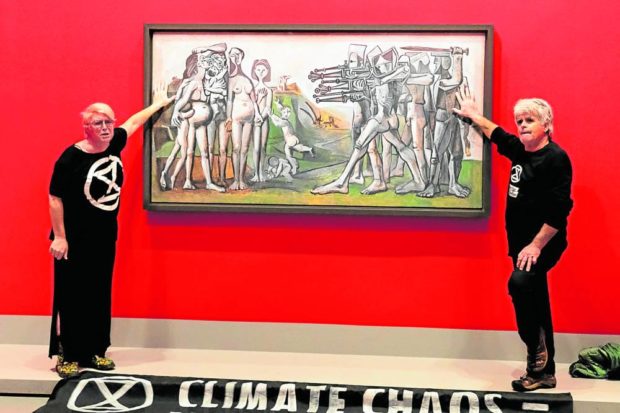 NEW CONTEXT FOR PICASSO This photo from environmental movement Extinction Rebellion shows climate activists with their hands glued to the perspex covering Pablo Picasso’s 1951 antiwar masterpiece “Massacre in Korea” at the National Gallery of Victoria in Melbourne. —EXTINCTION REBELLION/AFP