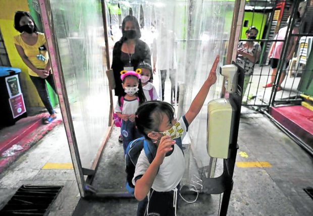 SCHOOL’S BACK Students pass through a booth for disinfection and temperature check at Aurora Quezon Elementary School in San Andres, Manila, during the first day of limited in-person classes in August. —RICHARD A. REYES. STORY: So far, no COVID clusters detected in schools – DOH