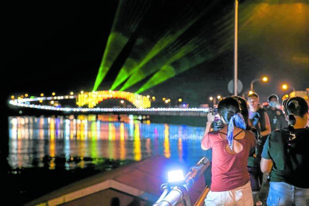 Residents watch and take photos of San Juanico Bridge from a distance during the switch-on ceremony for a light and sound show 