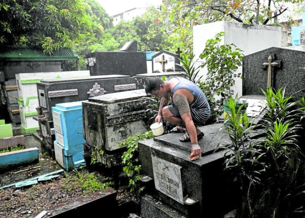 Despite the bad weather, a man cleans the grave of his departed loved ones at Manila South Cemetery in Makati. STORY: 2 Manila cemeteries closed to visitors due to Paeng