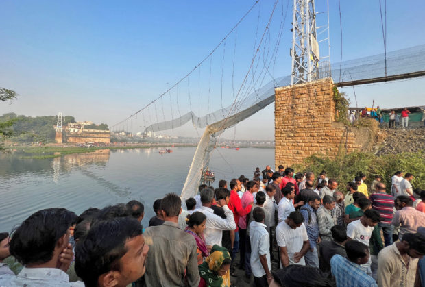 People gather as rescuers search for survivors after a suspension bridge collapsed in Morbi town