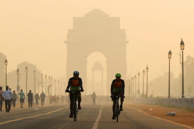 Men ride their bicycles in front of the India Gate shrouded in smog, in New Delhi