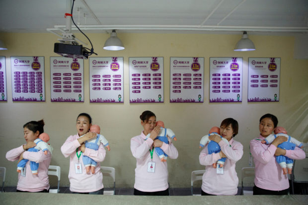 FILE PHOTO: Students at Ayi University, a training program for domestic helpers, practice on baby dolls during a course teaching childcare in Beijing