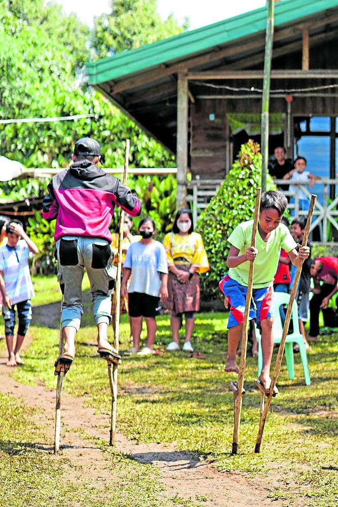  Children on wooden stilts known as “karang-karang” pass by each other during a two-team relay race, in the same way as their forefathers played outdoors and had fun in their younger years.