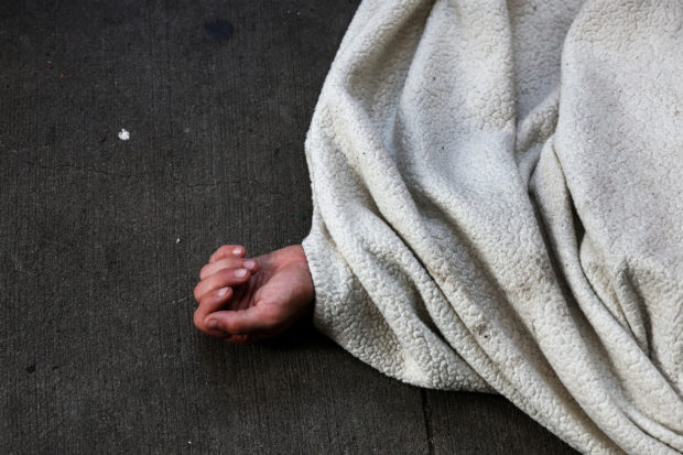 FILE PHOTO: A person sleeps under a blanket on the sidewalk along 42nd Street in New York City