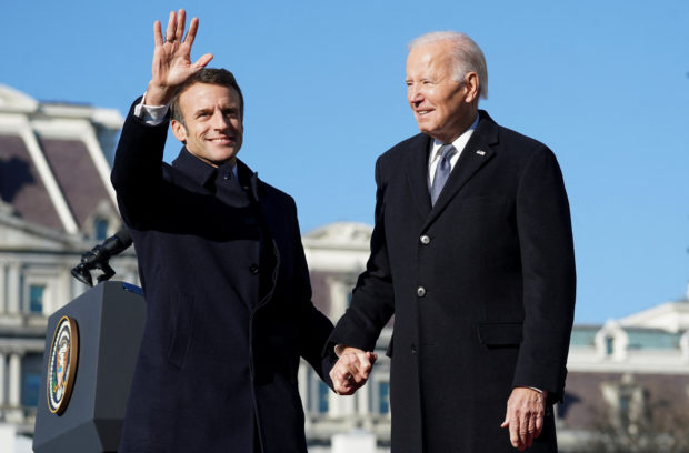 French President Emmanuel Macron waves as he holds U.S. President Joe Biden's hand onstage during an official State Arrival Ceremony for Macron on the South Lawn of the White House in Washington, U.S., December 1, 2022. REUTERS/Kevin Lamarque