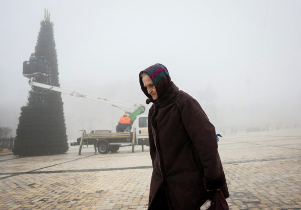 An old woman walks at the Sofiyska square as municipal workers install a Christmas tree during a heavy fog, amid Russia's invasion of Ukraine, in Kyiv, Ukraine December 17, 2022.  REUTERS/Gleb Garanich