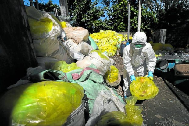 Dressed in personal protective equipment,a janitor at the storage area of Tala Hospital in Caloocan segregates trash bags, many of which contain infectious waste. 