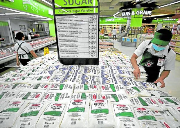 A grocery worker arranges sugar packs around a price reference board.