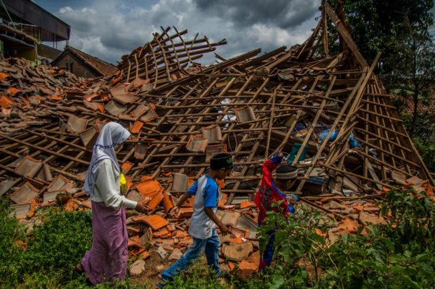 Children of earthquake victims walk past a collapsed house at Cugenang village in Cianjur, West Java on December 1, 2022, ten days after a 5.6-magnitude earthquake left 328 people dead. (Photo by ADITYA AJI / AFP)