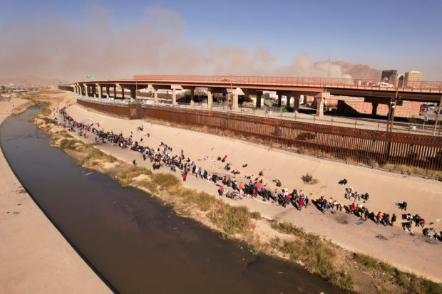 Migrants queue near the border wall after crossing the Rio Bravo river, in Ciudad Juarez