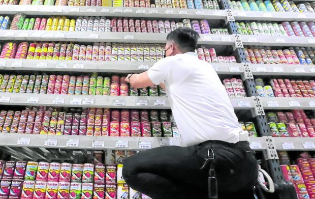 Man arranging canned goods on a store shelf. STORY: DTI approves price increases for bread, canned goods. 