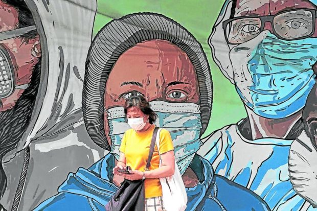 END IN SIGHT / SEPTEMBER 15, 2022 A pedestrian tinkers with her mobile device behind a mural of people wearing face mask in Eastwood Mall in Libis, Quezon City on Thursday, September 15, 2022. The world has never been in a better position to end the COVID-19 pandemic, the head of the World Health Organization (WHO) Director-