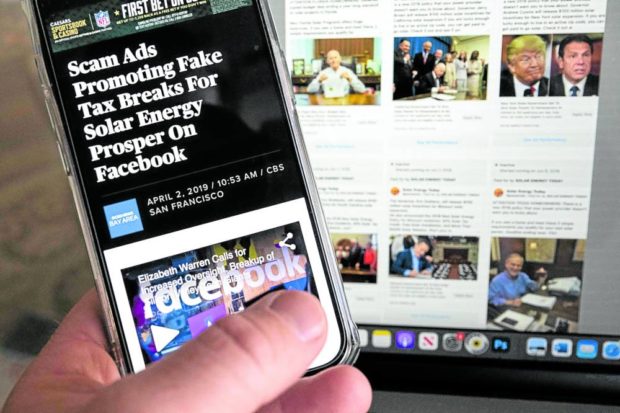 An illustration photo taken on Feb. 6 shows a phone screen displaying a story about scam ads promoting fake tax breaks for solar energy in front of a screen showing some of the Facebook archived fake ads luring people into the scam. STORY: Energy scammers cast ‘wide net’ on Facebook