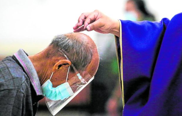 CHANGE IN PRACTICE At a Mass in February 2021, the second year of the pandemic, a priest sprinkles ash over the head of a churchgoer. —MARK ALVIC ESPLANA