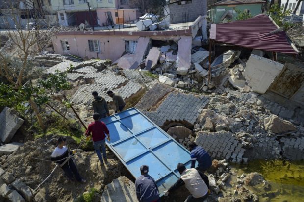 Four men carry a metal frame along a destroyed cobbled street in Demirkopru, a small Turkish village now divided by a large crack in Hatay on February 18, 2023. A 7.8-magnitude earthquake hit near Gaziantep, Turkey, in the early hours of February 6, followed by another 7.5-magnitude tremor just after midday. 