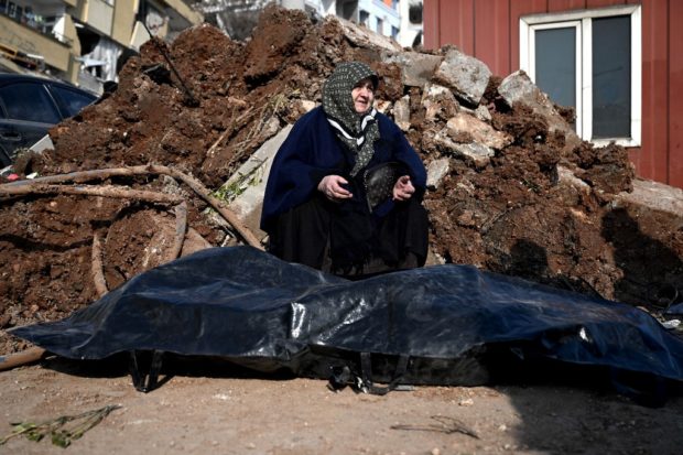 A woman sits next to the body of her nephew in Kahramanmaras, on February 9, 2023, three days after a 7,8-magnitude earthquake struck southeast Turkey. - The death toll from a huge earthquake that hit Turkey and Syria climbed to more than 17,100 on February 9, as hopes faded of finding survivors stuck under rubble in freezing weather. (Photo by OZAN KOSE / AFP)