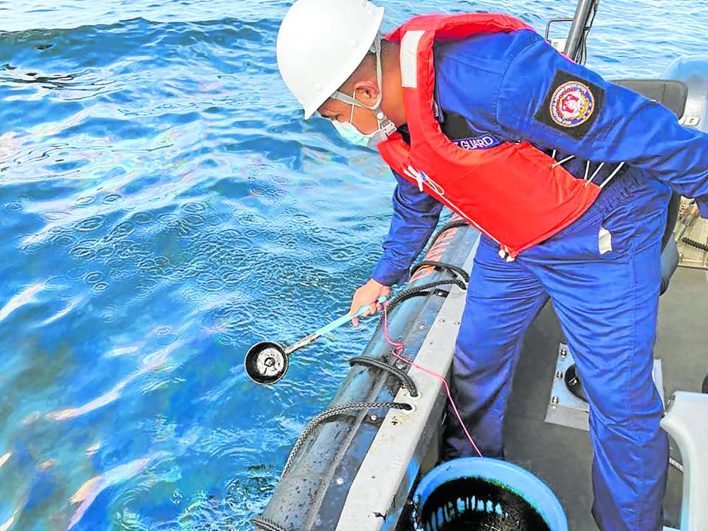 In this handout photo from the Philippine Coast Guard and taken on March 2, a coast guard personnel collects water samples from an area hit by oil spill off the waters of Naujan, Oriental Mindoro