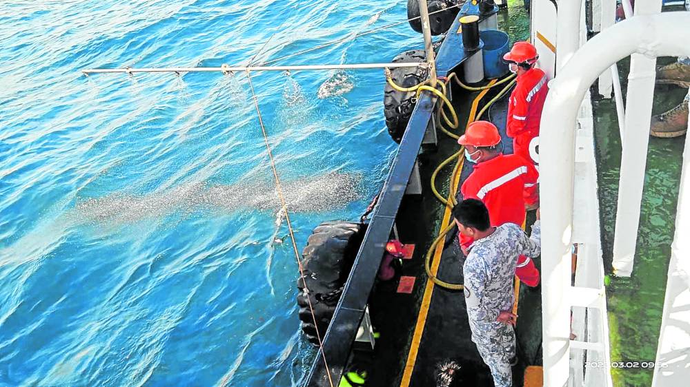Personnel of the Philippine Coast Guard (PCG) sprinkle chemicals to break down the oil that leaked from the sunken oil tanker Princess Empress in this PCG handout photo on Thursday