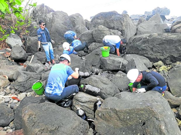 Volunteers from DMCI Power Corp. pick out, scrape and shovel industrial oil stuck to rocks in the shores of Barangay Misong in Pola, Oriental Mindoro, on March 3, 2023. STORY: Mindoro fishers bear brunt of oil spill