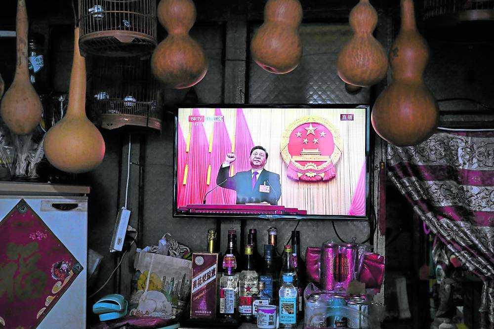 A TV screen at a convenience store shows live coverage as Chinese President Xi Jinping swears an oath after being reelected as president for a third term 
