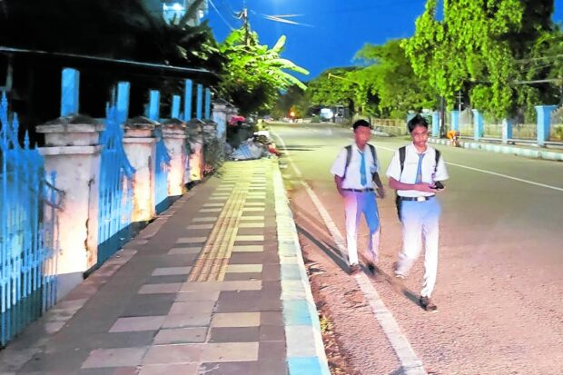 Two sleepy high school students walk to school in the early morning of March 6 in Kupang, Indonesia where a pilot project has twelfth graders from ten high schools starting classes at 5:30 am