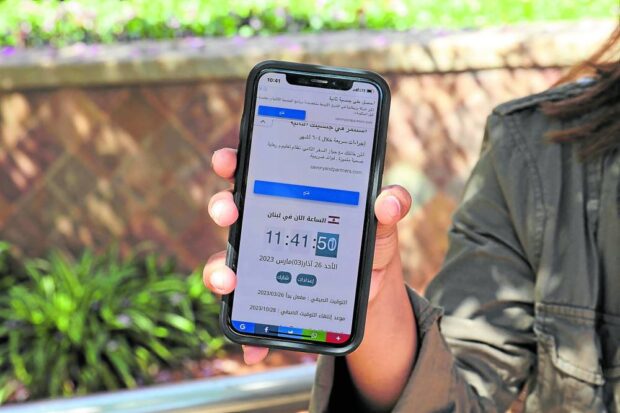 A woman in Beirut holds a mobile telephone showing contradicting time zones on March 26, 2023, after Lebanon’s government announced a decision to delay daylight savings. STORY: In times of crisis, Lebanese squabble over clock change