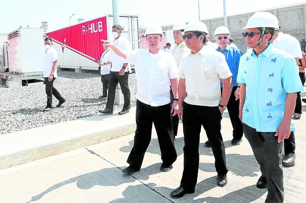 San Miguel Corp. CEO Ramon Ang pointsto President Marcos and Energy Secretary Raphael Lotilla (in blue shirt) the battery energy storage system facility of his company’s power armin Limay, Bataan, on Friday.
