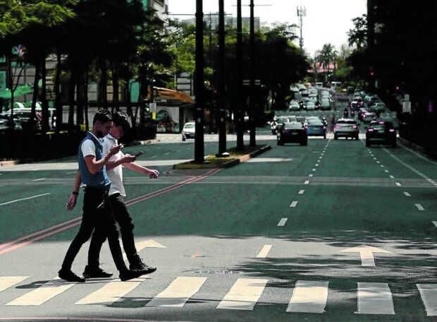 Two pedestrians use their cell phones while crossing a street in Taguig City. 
