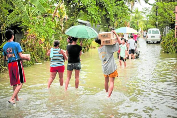 Residents of Barangay San Jose, Milaor town in Camarines Sur wade through a flooded street on their way home after receiving relief goods from the local government on Friday.