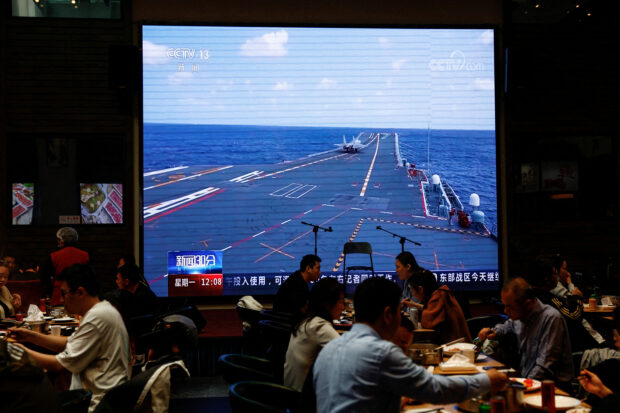 Customers dine near a giant screen broadcasting news footage of the Eastern Theatre Command of PLA taking part in an exercises around Taiwan, at a restaurant in Beijing