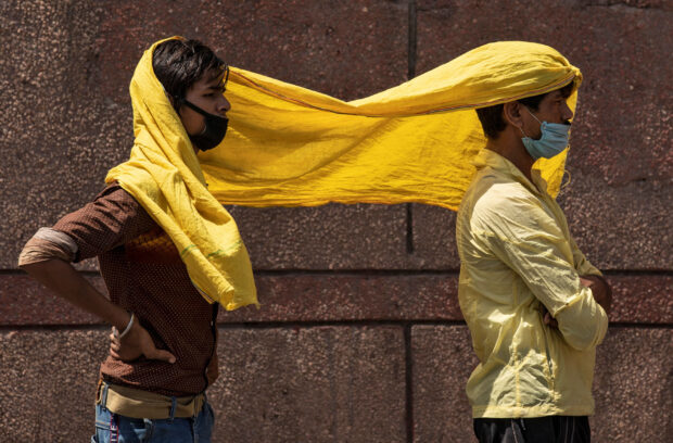 FILE PHOTO: Migrant workers cover themselves with a scarf, to protect from heat as they wait to get registered before boarding a train to their home state of eastern Bihar, during an extended lockdown to slow the spreading of the coronavirus disease (COVID-19), in New Delhi, India, May 21, 2020. REUTERS/Danish Siddiqui
